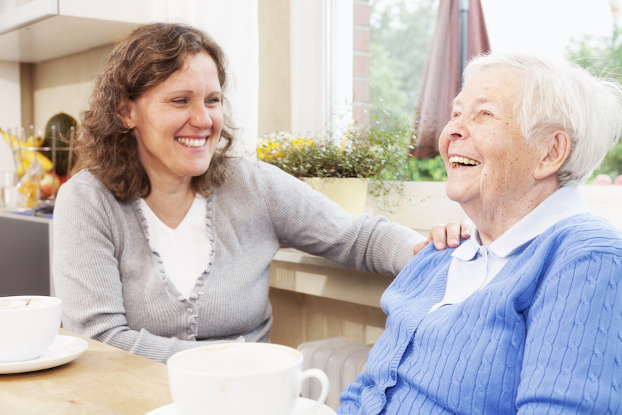 Adult daughter seated at the kitchen table in her senior mother’s home whilst drinking coffee over the holidays