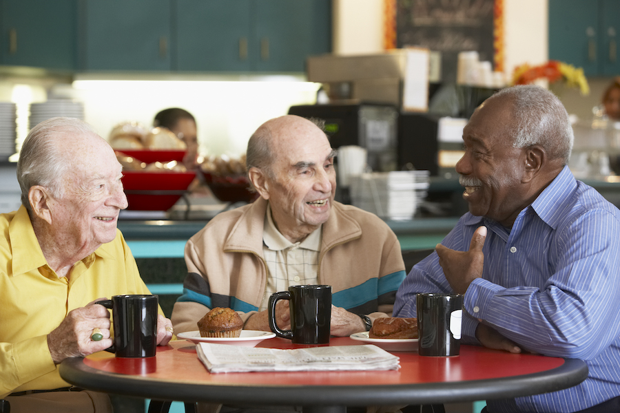 Three smiling senior men connect and socialize while drinking tea together and chatting at the senior living community