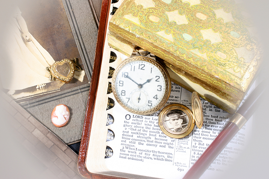 A keepsake box for an elderly loved one living with dementia containing an old pocket watch, picture locket, and cameo among vintage photographs and a fountain pen